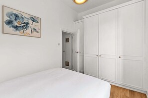 A bedroom with a large bed, white wardrobe, and a painting on the wall.