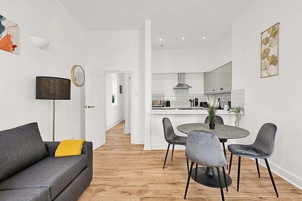 A modern living room with a grey sofa, a round dining table, and four grey chairs. A small plant is on the table.