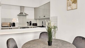 A modern kitchen with white cabinets, a stainless steel range hood, and a dining area with a round table and chairs.