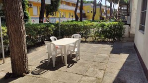 A courtyard with a table and chairs, surrounded by trees and a building with yellow and white walls. - Holiday home with air conditioning and washing machine (Rosolina Mare)