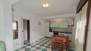 A compact kitchen with basic appliances, a dining area with a checkered floor, and a small dining table. - Holiday home with air conditioning and washing machine (Rosolina Mare)