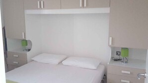 A bedroom with a bed, two nightstands, a green lamp, and a white wall. - Holiday home with air conditioning and washing machine (Rosolina Mare)