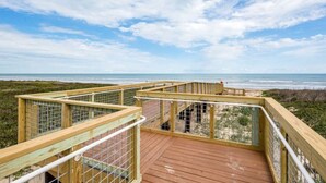 A wooden deck with a metal railing overlooking a beach.