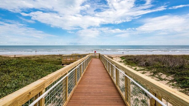 A wooden boardwalk leading to a beach with a clear sky.