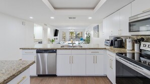 Una cocina moderna con armarios blancos, encimeras de granito, lavavajillas, estufa y microondas.