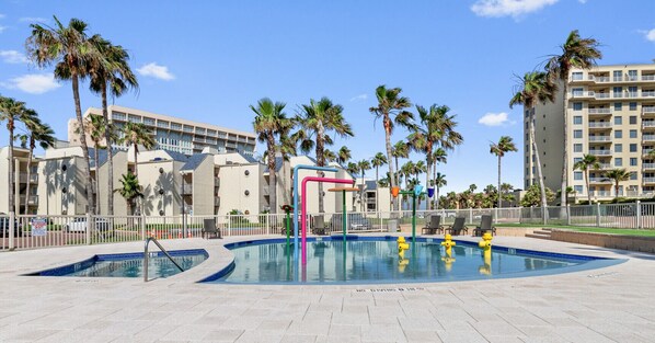 A swimming pool with a no diving sign, surrounded by palm trees and a multi-story building in the background.