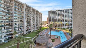 A high-rise hotel with multiple balconies, a swimming pool, and a well-maintained lawn.