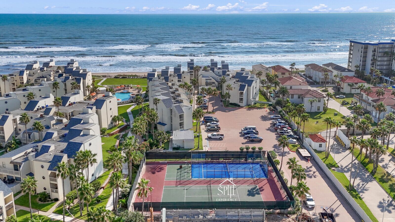 A coastal hotel with multiple buildings, a tennis court, and a view of the ocean.