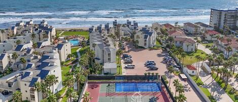 A coastal hotel with multiple buildings, a tennis court, and a view of the ocean.