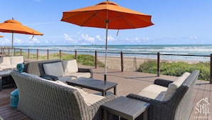 Eine Terrasse mit Korbmöbeln und orangefarbenen Sonnenschirmen mit Blick auf den Strand.