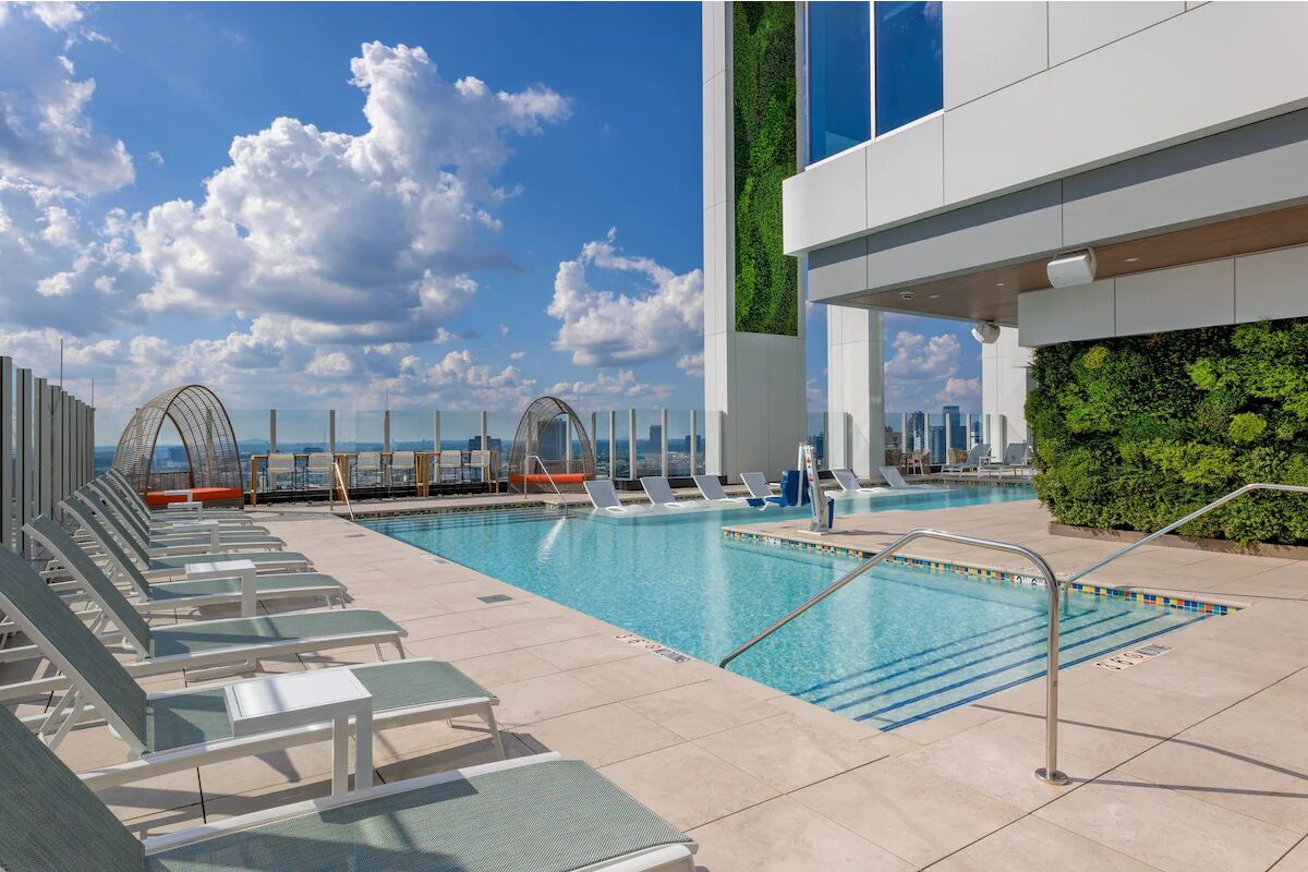 A rooftop pool with lounge chairs, a view of the city skyline, and a green wall.