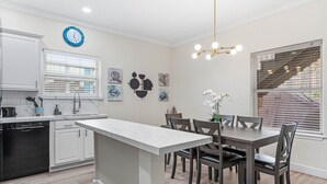 A modern kitchen with white cabinetry, a central island, and a dining area with dark wooden chairs and a table. - Ground Floor Beach Side 2Min Walk To The Beach SF (South Padre Island)