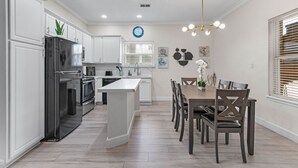 A modern kitchen with white cabinetry, a central island, and a dining area with a wooden table and chairs. - Ground Floor Beach Side 2Min Walk To The Beach SF (South Padre Island)