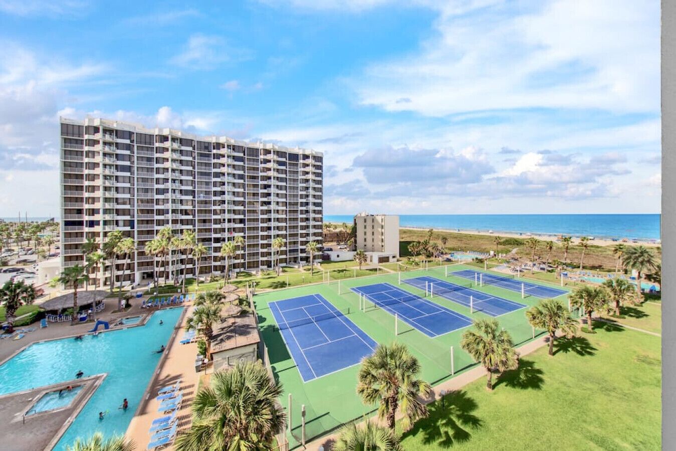 A hotel with multiple floors, a pool, tennis courts, and a beach view.