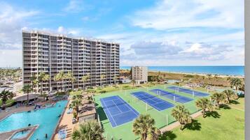A hotel with multiple floors, a pool, tennis courts, and a beach view.