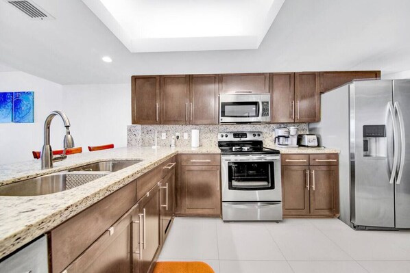 Una cocina moderna con encimeras de granito, electrodomésticos de acero inoxidable, armarios de madera y un tragaluz.