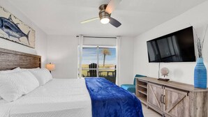 Ein Schlafzimmer mit einem Bett, einem Deckenventilator, einem Fernseher, einem Schreibtisch und einem Fenster mit Jalousien.