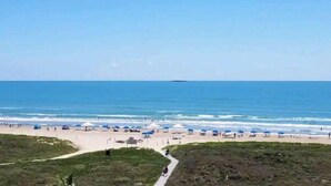 Ein Strand mit blauem Himmel, einem Weg zum Wasser und Sonnenschirmen am Ufer.