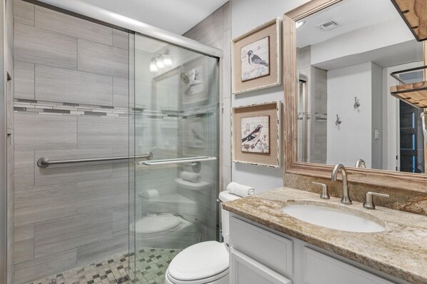 Un baño moderno con cabina de ducha de vidrio, inodoro blanco, lavabo con encimera de mármol y cuadros en la pared.