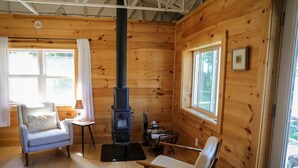 Ein gemütliches Blockhaus mit Kamin, zwei Sesseln, einem kleinen Tisch und großen Fenstern.