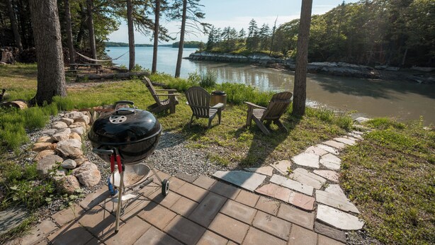 Eine Terrasse mit Grill, Stühlen und Blick auf einen See.
