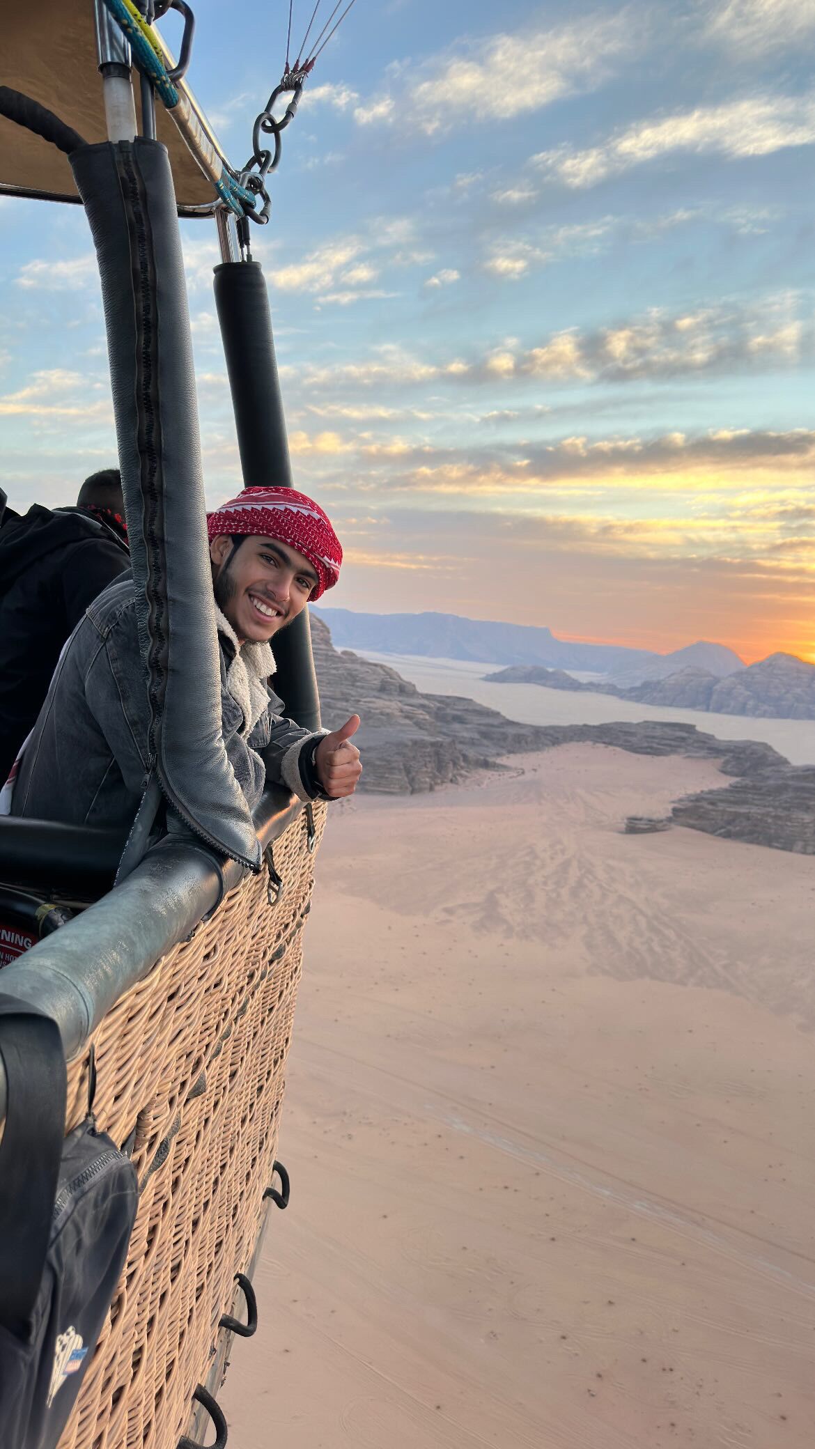 A person seated in a vehicle with a view of a desert landscape and mountains in the background.