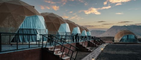 A row of geodesic dome tents with a stone pathway leading to them, set against a mountainous backdrop.