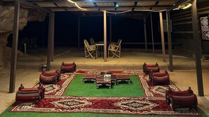 Un espacio al aire libre techado con una mesa central y sillas, rodeado de asientos acolchados rojos.