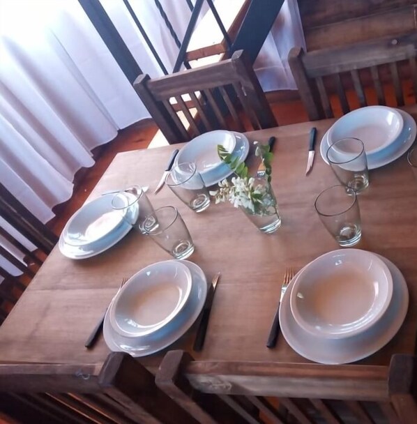 Una mesa de comedor de madera dispuesta con platos, cubiertos y vasos, con un jarrón de flores en el centro.