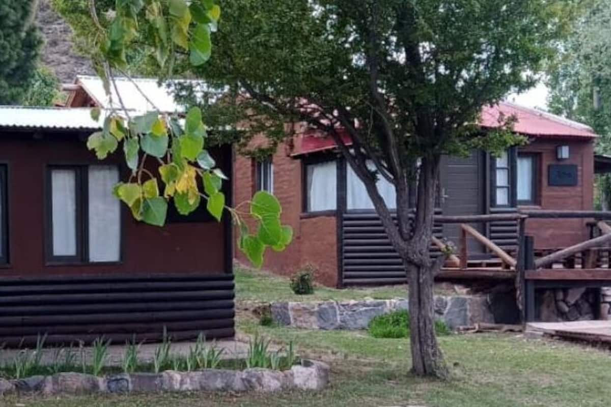 A rustic cabin-style building with a metal roof, surrounded by a wooden deck and a small garden area with yellow flowers.