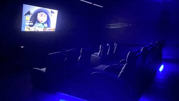 A dark room with a large screen displaying a cartoon character, rows of seats, and blue ambient lighting.