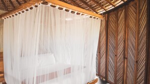 Een kamer met een bed dat bedekt is met een doorschijnende witte hemel, houten vloer en een houten scheidingswand met een geometrisch patroon.