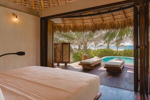 A bedroom with a bed, a wooden bench, and a view of a pool and palm trees. - Aldea Mizul (Villa de Tututepec de Melchor Ocampo)