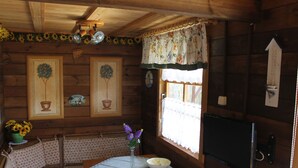 Et træhytteinteriør med et spisebord, stole, en vase med blomster og et vindue med gardiner.