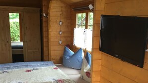 Une chambre dans un chalet en bois, avec un lit, des oreillers, une télévision et une fenêtre.