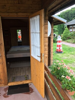 A wooden cabin with a bed, a small porch, and a garden with flowers and a lighthouse model. - Vacation cottage Möwe Binz (Binz)