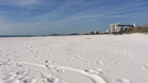 Una playa cubierta de nieve con huellas y edificios al fondo.