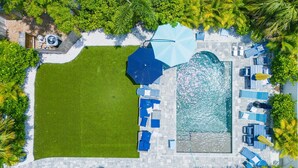 Vista aérea de un complejo turístico con piscina, tumbonas y una sombrilla grande.