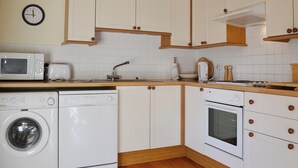 A compact kitchen with a washing machine, microwave, toaster, sink, and oven. - 2 bedroom accommodation in Oswestry (Oswestry)