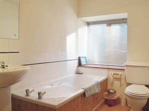 A bathroom with a bathtub, sink, toilet, and window with blinds.