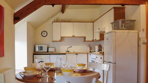 A kitchen with white cabinets, a microwave, a sink, and a refrigerator. There is a dining table with chairs and a clock on the wall. - 2 bedroom accommodation in Oswestry (Oswestry)