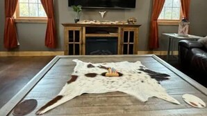A living room with a flat-screen TV mounted on the wall, a fireplace with a mantel, and a large leather couch. - Rustic Acres Cabins (Dieterich)