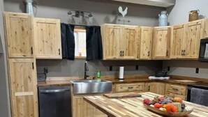 A kitchen with wooden cabinets, a stainless steel sink, a refrigerator, and a bar area with stools. - Rustic Acres Cabins (Dieterich)