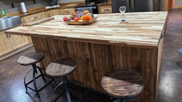A kitchen island with a wooden top and two stools. - Rustic Acres Cabins (Dieterich)