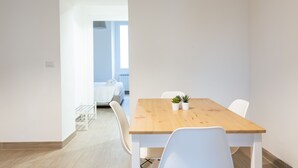 A modern, minimalistic room with a wooden dining table, white chairs, and two potted plants. - Moscova Modern Apartment  (Milan)