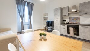 A modern kitchen with grey cabinets, a wooden dining table, and a TV in the background. - Moscova Modern Apartment  (Milan)