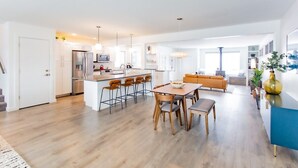 A modern kitchen with white cabinets, a central island with bar stools, and a dining area with a wooden table and chairs. - Bridger Hawk Duplex (NEW) (Bozeman)
