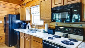 A kitchen with wooden cabinets, a black refrigerator, a microwave, a stove, and a sink. - Tennessee Cabin w/ Balcony, Hot Tub & Pool Access! (Sevierville)