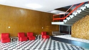 A lobby with a checkered floor, red seating, a staircase, and a textured wall. - Mundial Hotel Goiânia (Goiânia)
