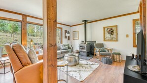 A cozy living room with a fireplace, comfortable seating, and large windows offering a view of the outdoors. - Ruidoso Rental w/ Private Hot Tub: Walk to Midtown (Ruidoso)